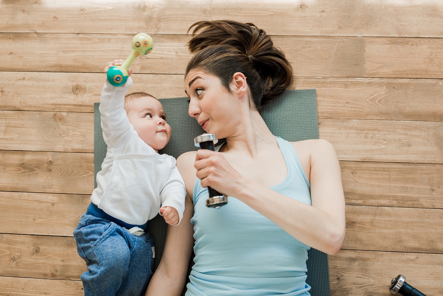 mother with baby boy lying on floor and playing with dumbbells